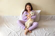 © Natasha  - A happy little brunette girl in purple pajamas, with her dark hair loose, sits hugging a white charming cat