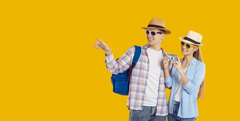 Happy young couple of Caucasian sightseeing tourists with camera traveling abroad on weekends. Joyful young man and woman in summer casual clothes looking at copy space on orange background. 