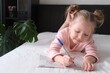 Portrait of a schoolgirl solves children crosswords on the bed. Logic games at home. Children solves crossword