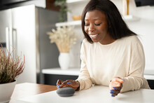 Charming Young African-American Young Woman Is Using Voice Commands For Wireless Smart Speaker Control. Smart Home And Technology Concept
