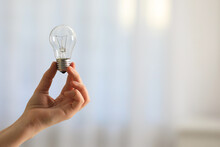 Woman Holding Light Bulb On Blurred Background, Closeup. Space For Text