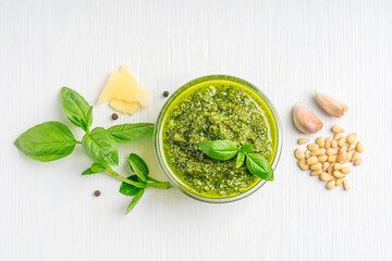 Wall Mural - Top view of Italian genovese local herbal pesto sauce made of blended parmesan cheese, green basil leaves, pine nuts, garlic, black pepper and olive oil served in glass bowl on white wooden background