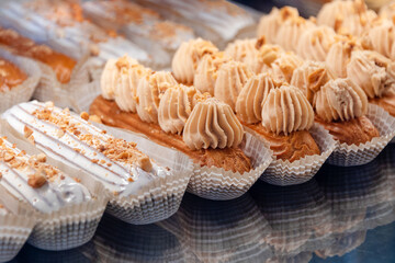 Eclairs on the shelf of a pastry shop or cafe. Tasty french sweets on window shop, delicious pastries for coffee. Cakes in pastry shop, variety of desserts with creamy topping on display in bakery