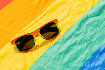 sunglasses with lgbt pride rainbow flag colors on lgbt pride flag background. summer and gay pride day concept.