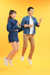 Wall Mural - Young excited asian people man and woman jumping isolated over yellow background