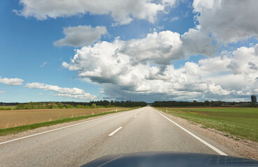 An empty highway (new asphalt road) through the field and forest. Dramatic storm clouds before the rain. Tourism, road trip, freedom, vacations, logistics, remote places concepts