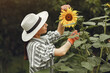 Woman in a hat and gloves standing near sunflowers