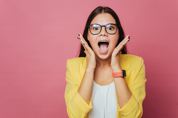 Portrait of a shocked young brunette girl in yellow jacket with wide open mouth and eyes amazed because the black Friday coming soon, over pink background with copy space. Discount and sales..