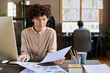 © pressmaster - Serious businesswoman in eyeglasses sitting at office desk with computer and examining charts in documents
