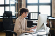 © pressmaster - Serious young businesswoman in eyeglasses sitting at office desk in front of computer monitor and typing on computer key