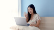 © Ekkasit A Siam - Beautiful Asian girl, wearing a white floral shirt, is video call chatting with friends on a laptop computer, on vacation chilling in his bedroom, greeting and chatting happily.