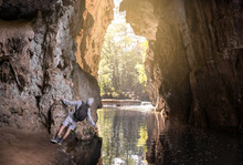 Unrecognizable Man Wearing A Hoodie And Carrying A Bag Is Having Fun Watching The River Passing By Through A Cave