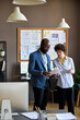 © pressmaster - Young businesswoman pointing at document and discussing it with her colleague, they standing at office and working in team