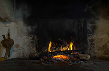 A Stone Open Fireplace With A Live Wood-burning Flame And An Antique Fire-blowing Device.