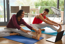 Diverse Gay Male Couple Smiling While Performing Stretching Exercise Together At Home