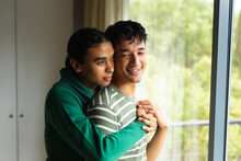 Diverse Gay Male Couple Hugging Each Other Standing Near The Window At Home