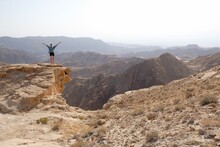 Silhouette Of Standing Woman With Arms Raised  On Rock At Beautiful Mountain Viewpoint. Views Of Mountain Range From Tafilah Highway, Dead Sea Depression In The Background. Jordan.