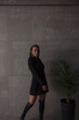 © NASTYA PALEHINA - teen fashion. young girl in black slim dress-jacket and over the knee boots stands casual in step and looking down on the gray loft wall background with plant palm. lifestyle concept, free space