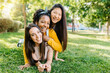 © Xavier Lorenzo - Happy young women best friends having fun together outdoors - Three united multiracial female on top of each other lying on grass in public city park - Female friendship concept - Copy space