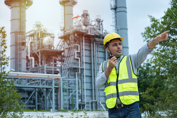 worker talking on the radio communication. industrial engineer in Oil factory. Engineer wearing PPE uniform and helmet looking detail tablet on hand with power plant  on background.