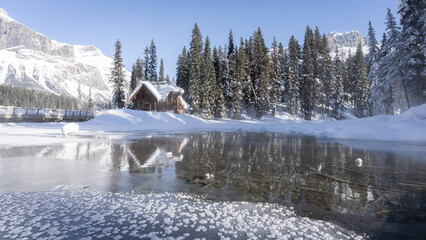 Wall Mural - Small hut on the bank of frozen lake surrounded by mountains with and forest, Yoho N. Park, Canada