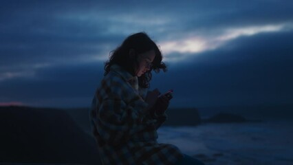 soft focus on dreamy millennial girl sits on ocean shore on dark warm windy night at porto, looks at