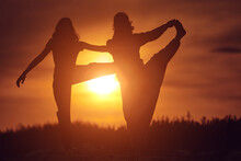 Mother And Daughter Practicing Yoga Together In Sunset Sunrise Time In Nature.