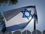Fototapeta  - The flag of the State of Israel against the blue sky, mounted on the fence of a private house.
