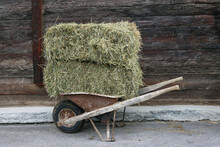 An Old Cart Loaded With Straw Bales, Standing In Front Of A Wooden Wall.