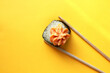 Fresh sushi roll, isolated on a yellow background. One sushi rolls are between the chopsticks. Asian cuisine. Copy space. Top view. Flat lay. Meal