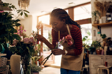 Wall Mural - Creative black florist arranging flowers while working at her flower shop.