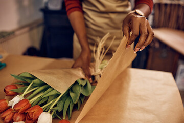 Wall Mural - Close up of female florist wrapping tulips in pack paper at flower shop.