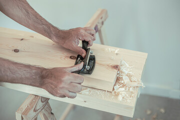 Two man's hands using a cabinet scraper to work on a wooden slat in an artisan workshop with natural light