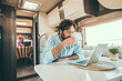 © simona - Couple use computer inside camper van during travel vacation or van life lifestyle. Modern man and woman work together on laptop in alternative office motor home. Digital nomad and smart free working