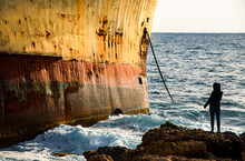 Person Looking At Moored Shipwreck On A Rocky Coast Line And Wind Waves. Paphos Cyprus