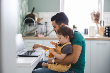 dad working on laptop with child sitting on his lap