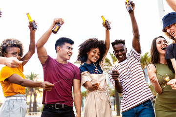 Wall Mural - Group of multiracial young friends having fun on summer party - Millennial people celebrating together with sparkles cheering with beers - Vacation and friendship concept - Focus on african couple