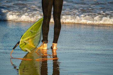 Wall Mural - view of surfers feet and green surfboard on the wet sand