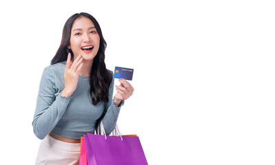 Excited asian showing credit card holding shopping bags in arm standing white background. Cheerful shopper girl using plastic card payment carrying shopping paper bags on sale over isolated background