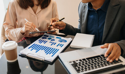 Businessman hand using laptop and tablet with social network diagram and two colleagues discussing data on desk as concept.