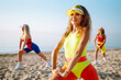 © maxbelchenko - Three young women in swimsuits are training on the beach. Beautiful women are dancing on the beach. Fitness, training, aerobics and people concept. Active sport.