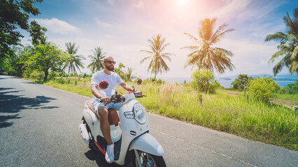 Wall Mural - Stylish young man rides a motorbike on the road near the sea and palm trees