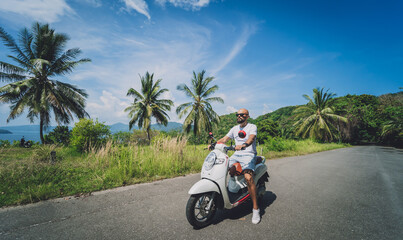 Wall Mural - Stylish young man rides a motorbike on the road near the sea and palm trees