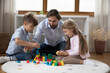 © fizkes - Dad and little children play wooden bricks at home. Preschool siblings enjoy playtime with loving caring father spend leisure together in modern cozy nursery. Family activity on weekend, fun concept