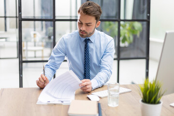 Sticker - Young man is working with papers while sitting in the office. Successful entrepreneur is studying documents with attentive and concentrated look.