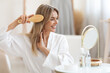© Prostock-studio - Smiling beautiful blonde woman combing hair at home