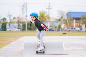 Child or kid girl playing surfskate or skateboard in skating rink or sports park at parking to wearing safety helmet elbow pads wrist and knee support