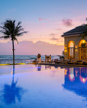 Couple Men And Women On The Beach During Sunset With Reflection In The Pool During A Luxury Vacation