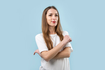 Wall Mural - Smiling young woman in white t-shirt with arms crossed on blue background