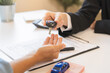 © KMPZZZ - Business car rental company service, Close up hand of agent dealer giving, holding car key to customer renter, new owner after signed rental, purchase contract in document, vehicle sales agreement.